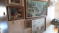 Photo shows a wall displaying all five framed needlepoint artworks, with varied subjects including wildlife, birds, and still life, all under glass in different sized frames.