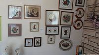 Wide wall view showing multiple framed needlepoint artworks hung in group, various sizes and styles focused on floral and animal themes.