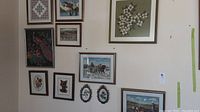 Full view of all 11 framed needlepoint pictures arranged on a wall in a grid pattern, showing multiple sizes and subjects including animals, flowers, and landscapes