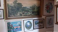 Multiple framed needlepoint artworks and one large framed print hung on wall, showing overall lot contents and framing.