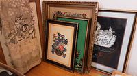 Full view of the five tapestries and needlepoint artworks, four framed and one rolled textile leaning against a wall.