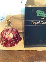 Porcelain figurine of Lady Victoria in a pink floral dress next to its original Royal Doulton box.