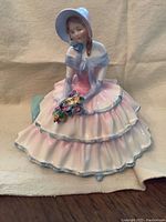 Front and side view of the Royal Doulton Daydream figurine showing pastel pink and blue dress, bonnet and flower detail in hands.