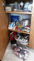 Three shelves in a wooden cabinet displaying many tailoring supplies including threads, zippers, buttons, and sewing notions.
