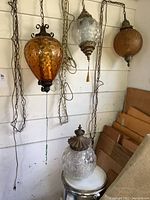 Four glass globe lamps against wall, three hanging on chains and one sitting on drum