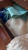Wool shawl in cream and blue-green pastel colors with fringed edges inside drawer with blue and white fabric.
