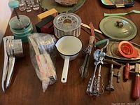 Photo showing the full assortment of vintage kitchen items on a wooden surface, including utensils, hand tools, and lids.