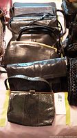 Overall view of approximately 10 vintage black purses arranged overlapping on a surface showing variety of styles and textured finishes.