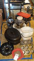 Photo showing assortment of bakeware and cookware including Corning Ware casserole pans with blue cornflower design, Pyrex covered dish, bundt cake pan, cupcake pans, cooling racks, and more.