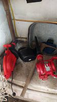 Red Black & Decker Leaf Hog, Toro Power Sweep, metal tub, pickaxe, and watering can stored on a floor corner, corded electric blowers visible.