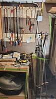 Wall-mounted metal clamps, large metal clamps on floor leaning against wall, and workbench below with various tools and clamps scattered
