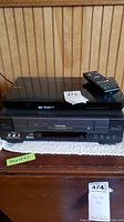 Stacked Sony Blu-ray player with remote on top of Toshiba VHS player, both black.