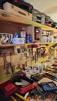 Photo showing pegboard with various tools including hand saws, measuring devices, clamps, and hammers.