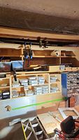 Photo showing wooden racks and storage containers filled with screws, nails, clamps mounted on shelf, and a workbench below.