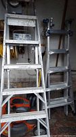 Full view of two aluminum ladders standing upright. One is a 5-way combination ladder with multiple hinges, the other a Werner step ladder.