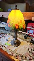 Metal lamp with scalloped base and yellow reverse painted floral glass shade featuring red roses and green foliage.