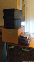 Wide shot showing boxes and a basket containing tapes and CDs on a tabletop