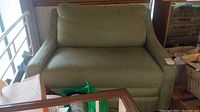 Front view of oversized green fabric chair with attached back cushion, showing overall condition and shape.