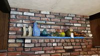 Wide view of two brick wall shelves displaying all items: onyx angel bookends, blue ceramic cat, blue ceramic cow, six glass paperweights, ceramic frog, bronze baby slippers.