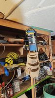 Photo of wooden shelves containing boxed and loose power tools including a hanging tool belt, yellow coiled air hose, and other miscellaneous tools.