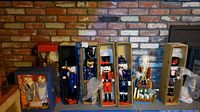 Front view of Raggedy Ann and Andy dolls in blue display box with six boxed nutcrackers and one loose nutcracker on a brick hearth