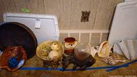Photo showing multiple items including a large dark wooden bowl, decorative bowls of metal, ceramic and live wood, glass bird figurines, ceramic owl vase, decorative balls, and three large seashells including a conch and starfish.