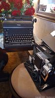 Shelf display of Royal manual typewriter and Sears film projector with floral background.