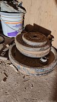 Stack of rusted metal weight plates of various sizes alongside a white bucket.