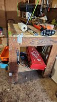 Handmade wooden work table holding tools and accessories, bottom shelf with Milwaukee Sawzall case visible