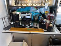 Overall display of assorted barware including rack, opener, ice bucket, and black organizer caddy with tools and coasters