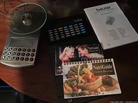 Beurer digital diet scale with glass weighing plate, keypad, LCD screen, NutriGuide booklets, and calculator on a table.