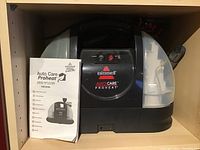 Front view of Bissell deep cleaner with instruction manual displaying model Auto Care ProHeat 1425 Series, showing water tanks and controls.