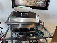 Photo of the full chafing dish top with lids and various accessories on a glass table including a small white bowl on top, candy dish, and napkin holder.