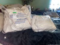 Quilted cooling mattress toppers or mattress covers in original clear packaging, labeled with cleaning directions, displayed on a bed.