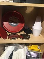 Overview of red plastic lid with removable grater discs and white utensil holder on wooden shelf
