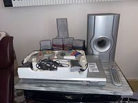 View of Durabrand HT-400 home theatre system components arranged including subwoofer, satellite speakers, remote control, and Super Joystick game console with controllers on top of a silver DVD player.