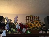Overview of faux flowers including sunflowers, roses, irises, and other mixed blooms arranged on a surface with two teddy bears at the sides.