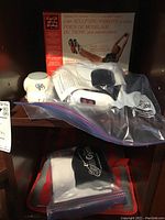 Photo showing core sculpting weights with the original box and additional massager device on a shelf.