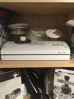 FoodSaver Vac 750 vacuum sealer with control buttons on top, sitting on shelf with accompanying accessories visible.