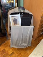 Photo showing the press with a jacket on the hanger and pants on the rack, with a printed photo of the press leaning against it.