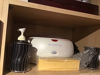 Remington heat treatment device with soap dispenser, toothbrush holder, and paraffin wax block on shelf