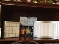 Photo showing a Berger lamp with a frosted rectangular grid panel and a small sculpture or decorative object beside it on a shelf.
