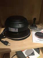 Michelangelo Crisp Top air fryer unit with power cord, metal mesh basket, rest pad, and instruction booklet displayed on shelf.