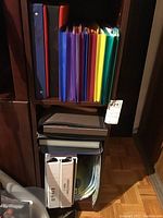 View of binders including white binders with photo pages, brown and black folders, and additional paper organizers stacked on lower shelf.