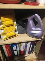 Shark SC630 portable steam cleaner in purple, yellow accessories, and black carrying bag on shelf