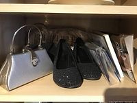 Shelf displaying two evening clutch bags, two pairs of black dress shoes with rhinestone embellishments, and two pairs of pantyhose wrapped in packaging