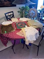 Photo showing various tablecloths, doilies, placemats, and salt and pepper shakers arranged on a table for sale.