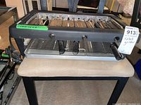 Front view of TFAL electric BBQ broiler kebob grill sitting on a beige bench, featuring multiple metal skewers, black body, and silver drip trays below.