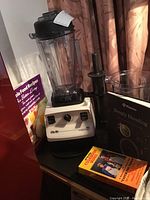 Overall view of Vitamix base with blending container, tamper, recipe books, and VHS video cassette