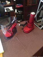 Wolfgang Puck red electric spiralizer main unit with attached clear plastic container and red accessory part on a table